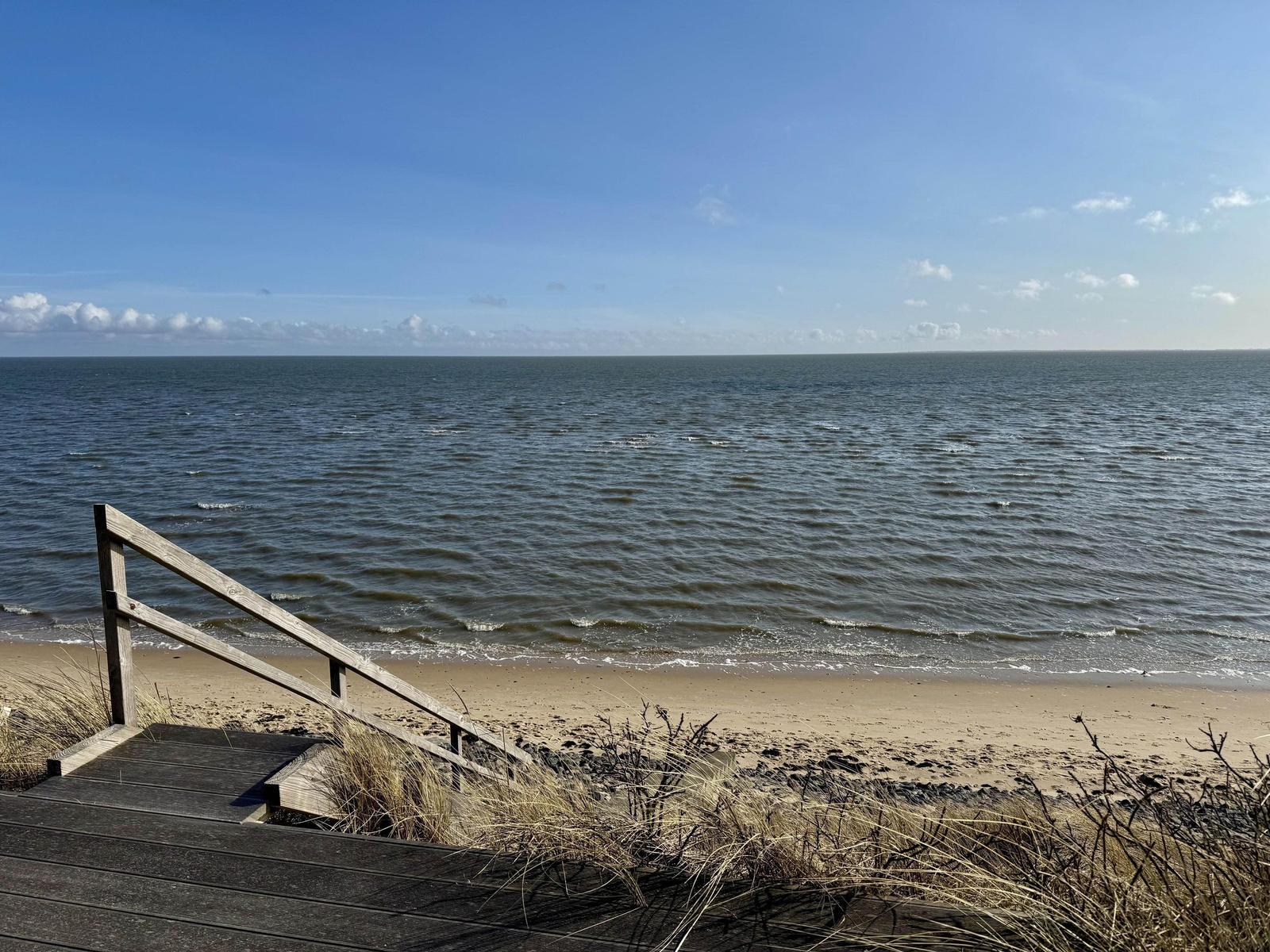 Holzsteg führt zum Strand. Meer und Himmel sind weit und klar.