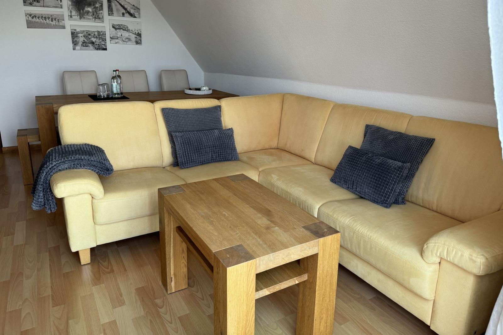 Ein Wohnzimmer mit gelbem Sofa, Holztisch und Wandbildern.