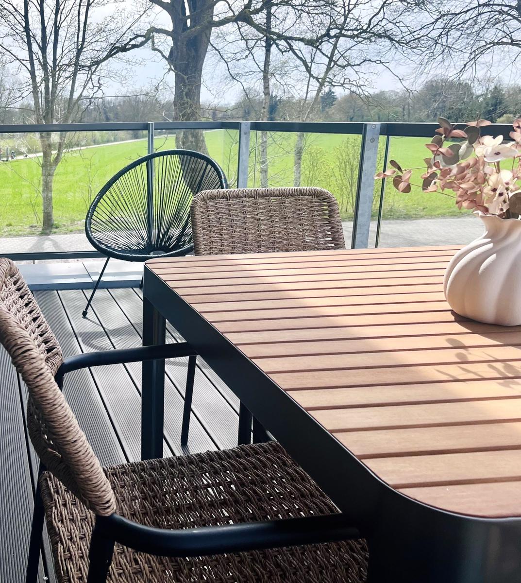 Terrasse mit Tisch und Stühlen, Blick auf grünes Feld und Bäume.