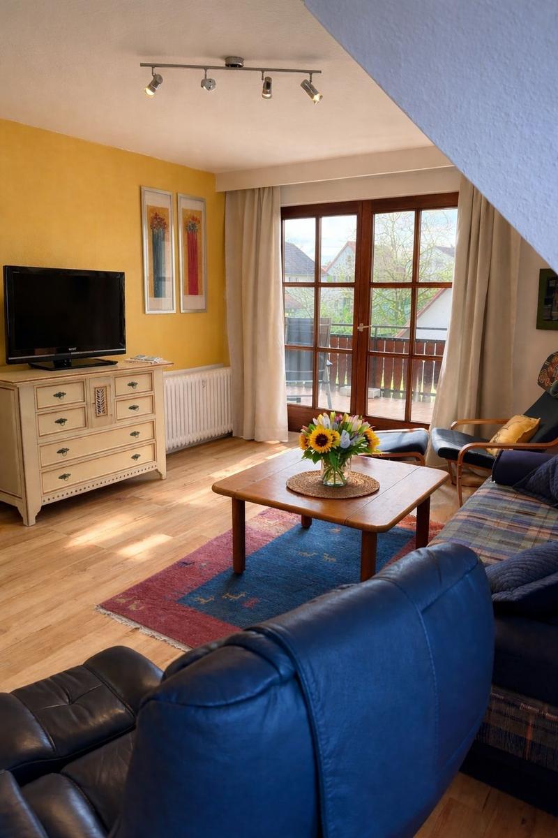 Wohnzimmer mit Sofa, Couchtisch und TV. Fenster mit Blick auf Balkon.
