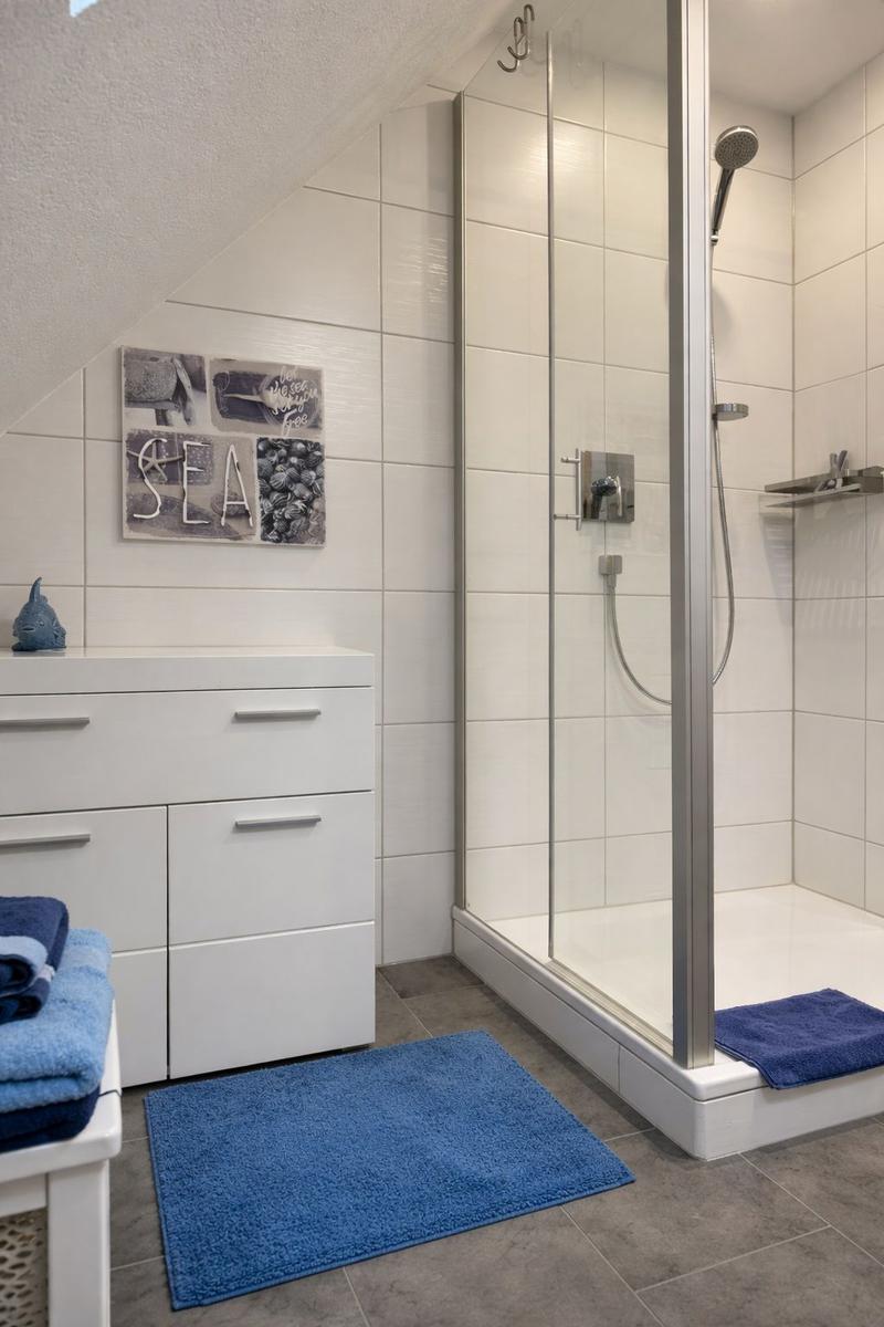 Badezimmer mit Dusche, Waschbecken und blauen Handtüchern.