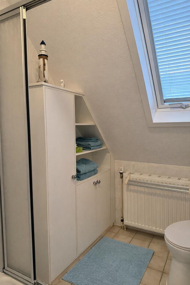 Badezimmer mit Duschabtrennung, Schrank und Fenster mit Jalousie.