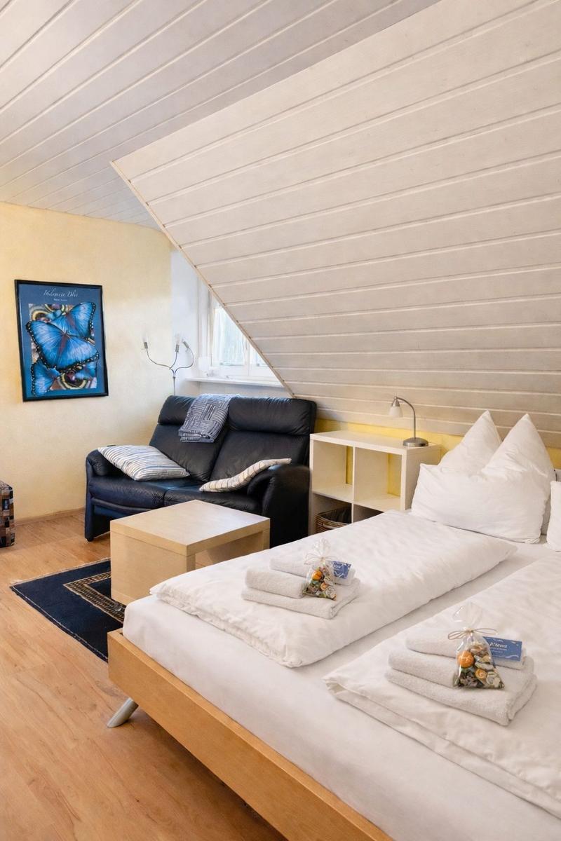 Schlafzimmer mit Doppelbett, Sofa und Holzboden unter schräger Decke.