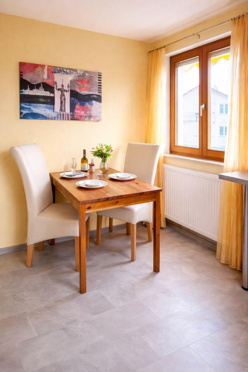 Esszimmer mit Holztisch, zwei Stühlen, Fenster und Wandbild.