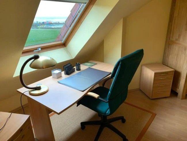 Schreibtisch unter Dachfenster mit Stuhl und Schreibtischlampe.