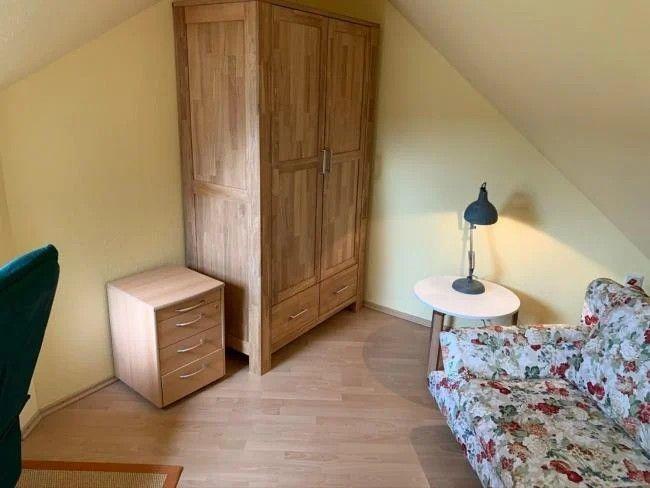 Schlafzimmer mit Holzschrank, Nachttisch und floralen Sofas.