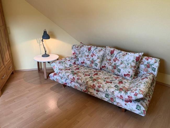 Ein Sofa mit floraler Bezugsstoffe steht in einem Raum mit Holzboden und schräger Decke.