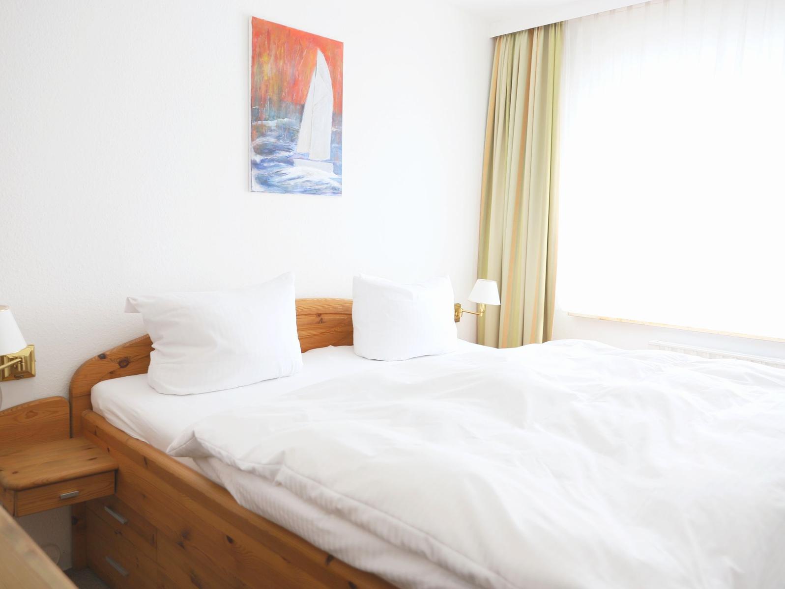 Schlafzimmer mit Bett, Nachttisch und Wandbild. Fenster mit Vorhängen.