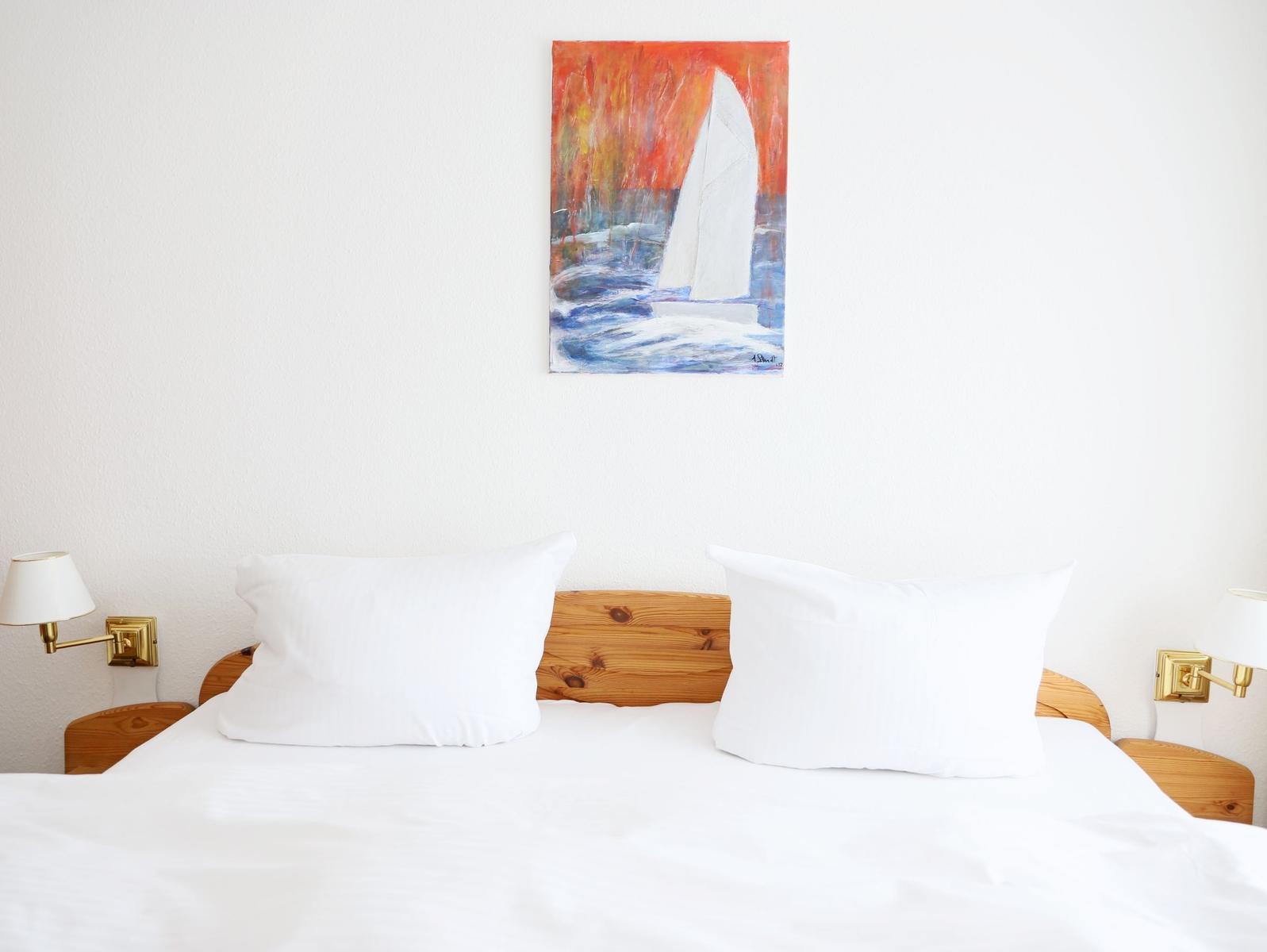Doppelbett mit weißen Kissen und Holzkopfteil. Wandbild mit Segelboot.