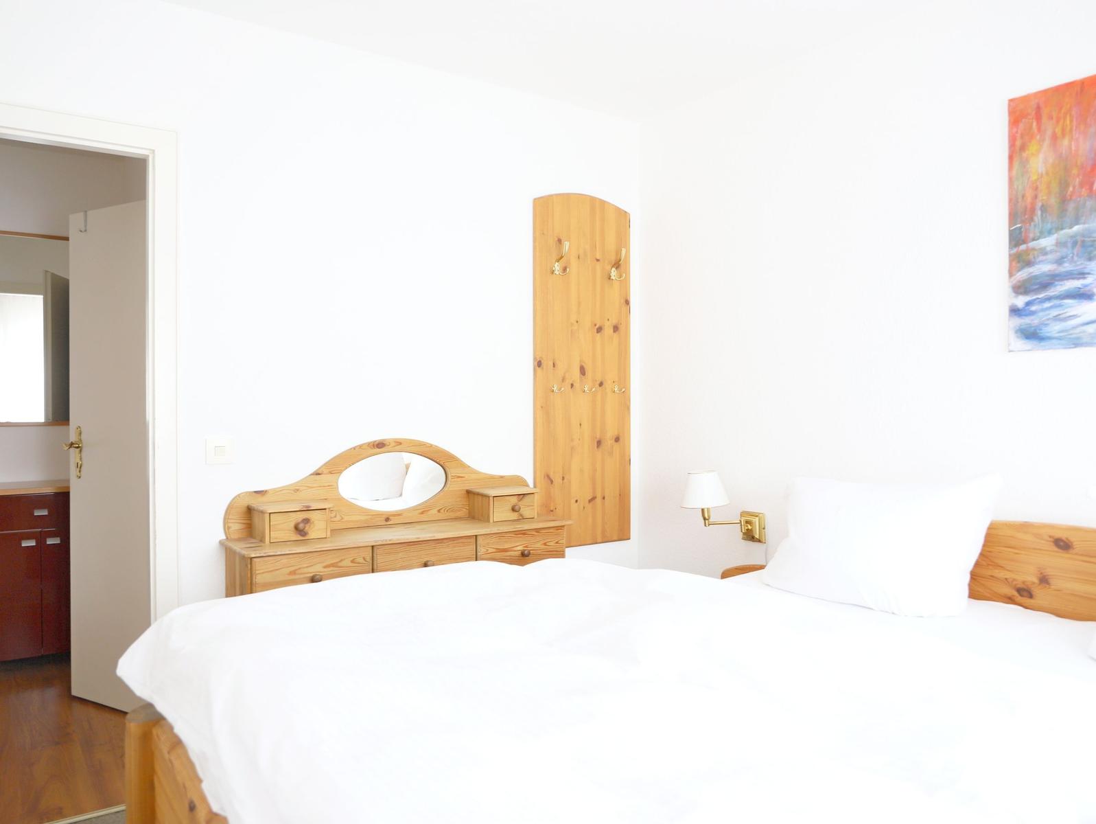 Schlafzimmer mit Holzbett, Schrank und Wandgarderobe. An der Wand hängt ein Bild.