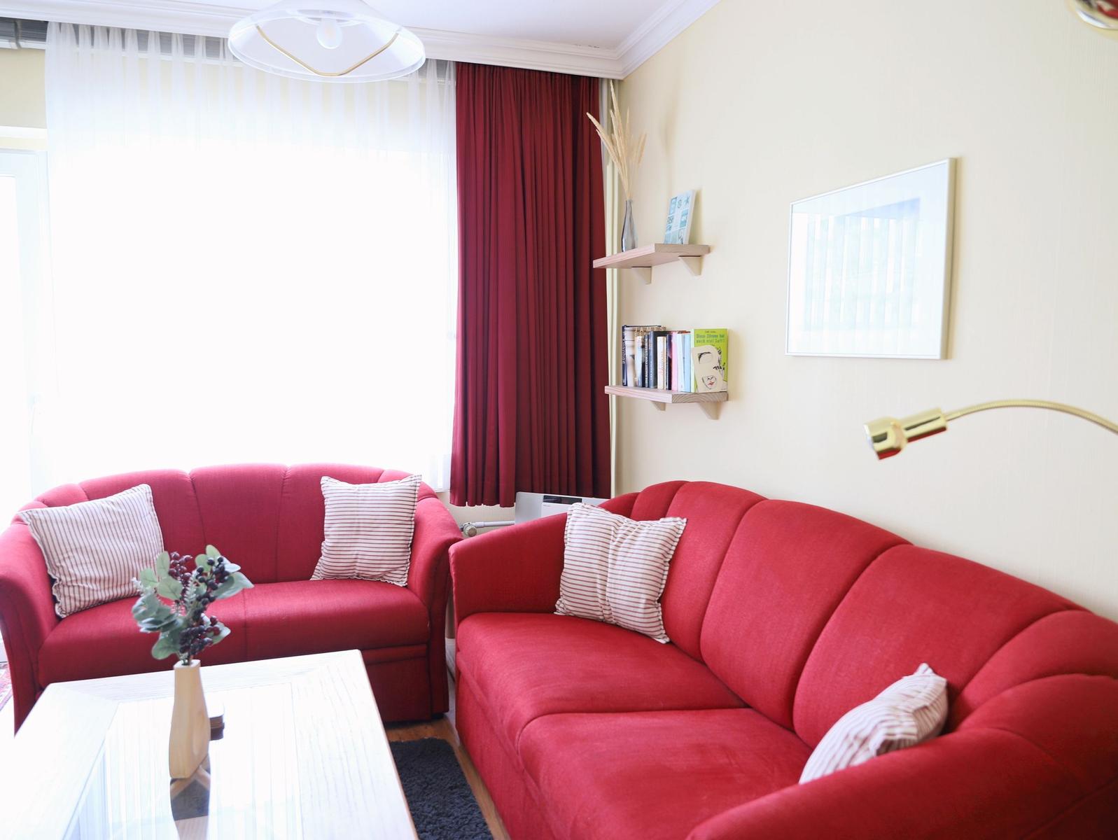 Zwei rote Sofas mit Kissen stehen im Wohnzimmer. An der Wand hängen Bücherregale und ein Bild.