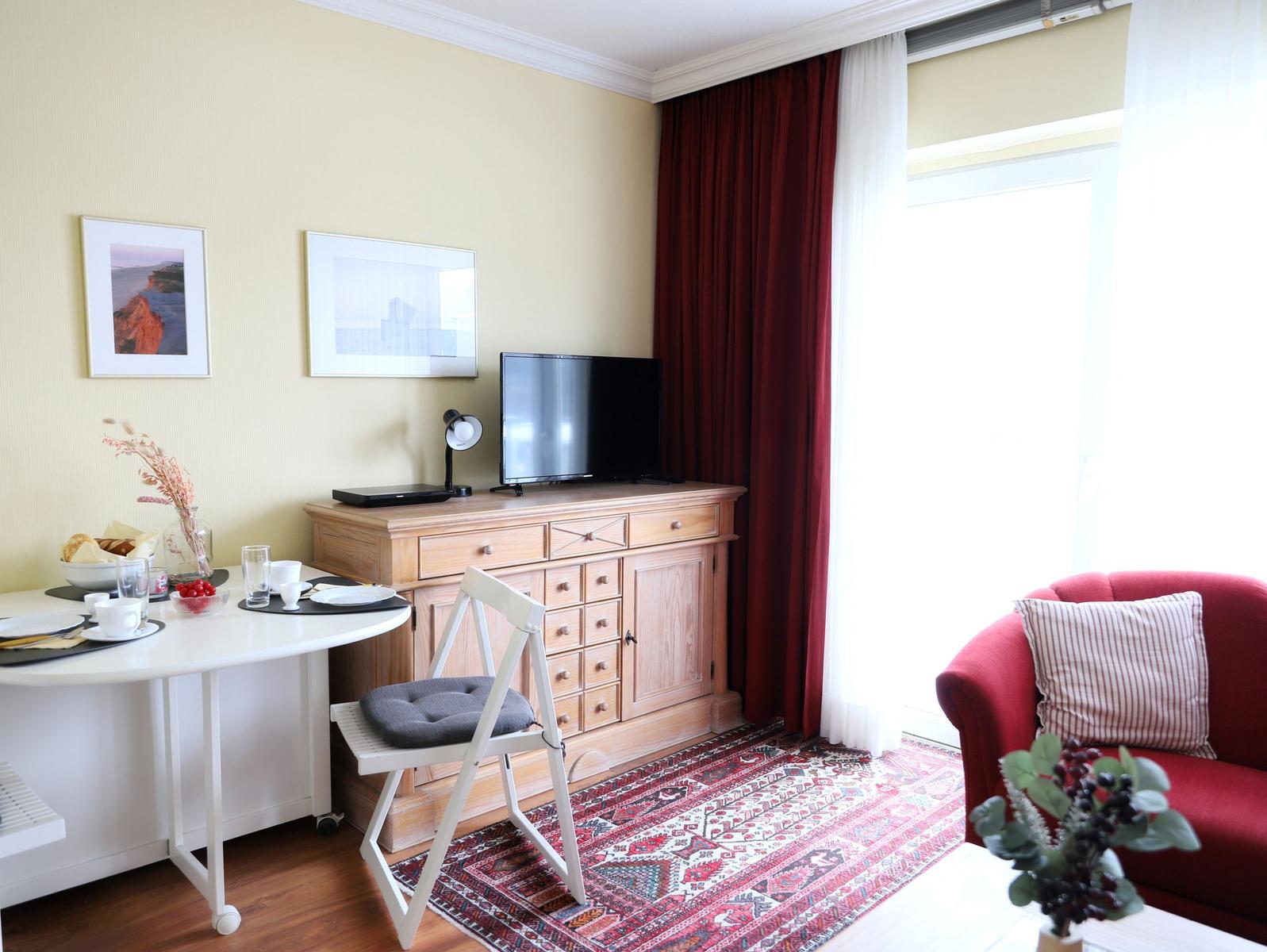 Ein Raum mit Esstisch, TV-Schrank, rotem Sofa und Teppich.