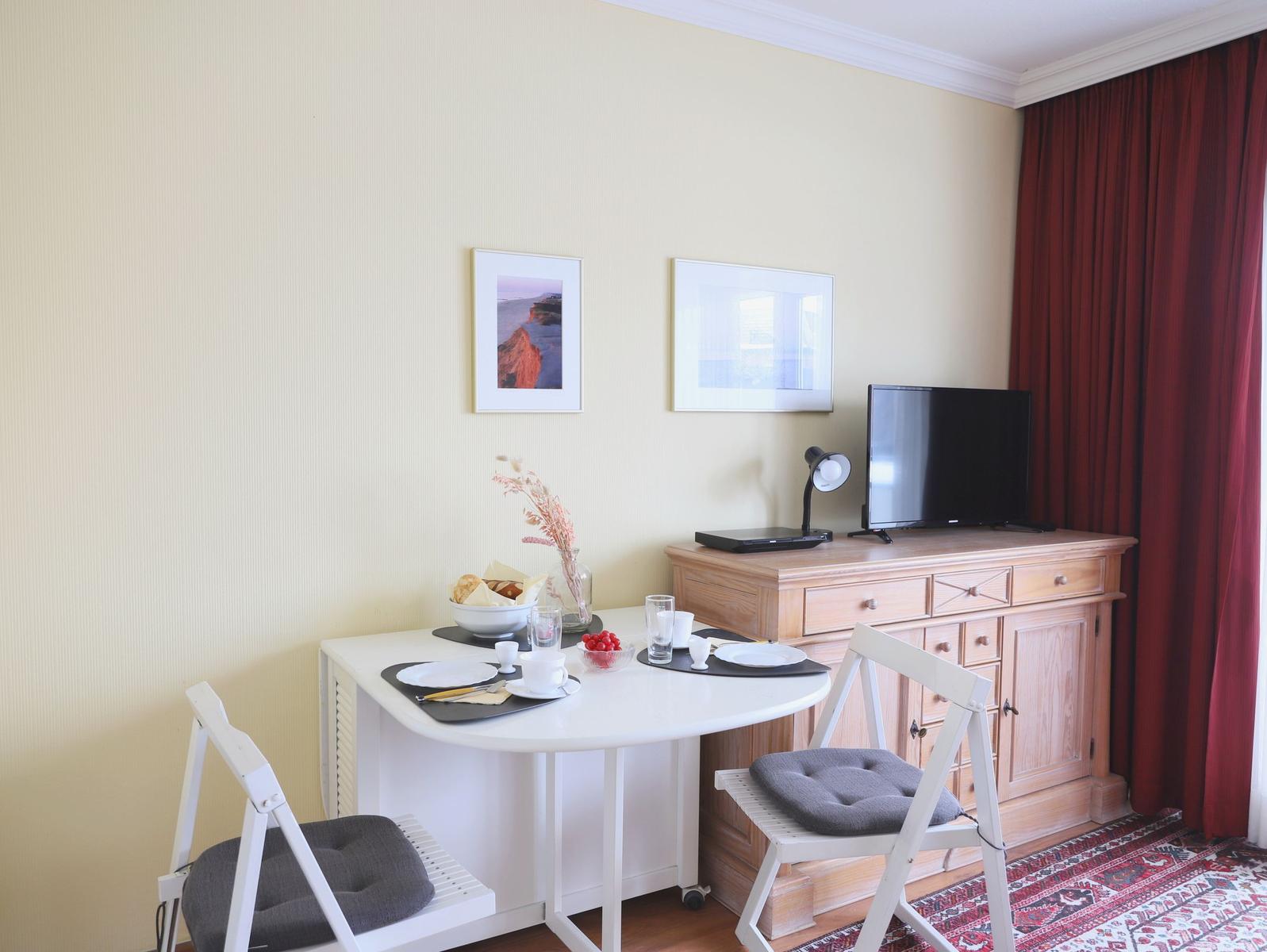 Essbereich mit Tisch, zwei Stühlen und Fernseher auf Schrank.