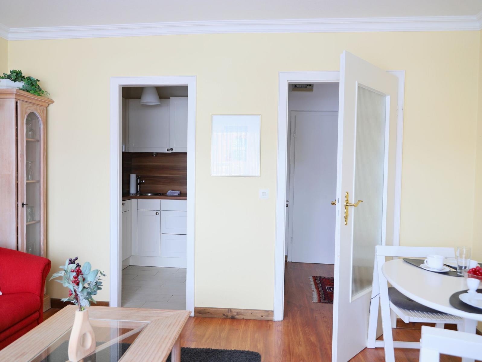 Wohnung mit Essbereich, Küche und Schlafzimmer. Holzboden, rote Couch und Esstisch.