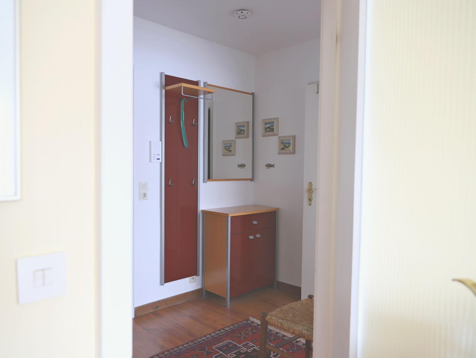 Eingangsbereich mit Kleiderschrank, Spiegelschrank und Holzschrank. Teppich und Stuhl sind sichtbar.
