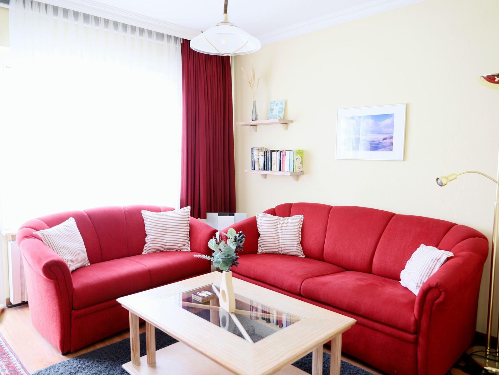 Zwei rote Sofas um einen Holztisch mit Glasplatte. Wandregale und ein Bild an der Wand.