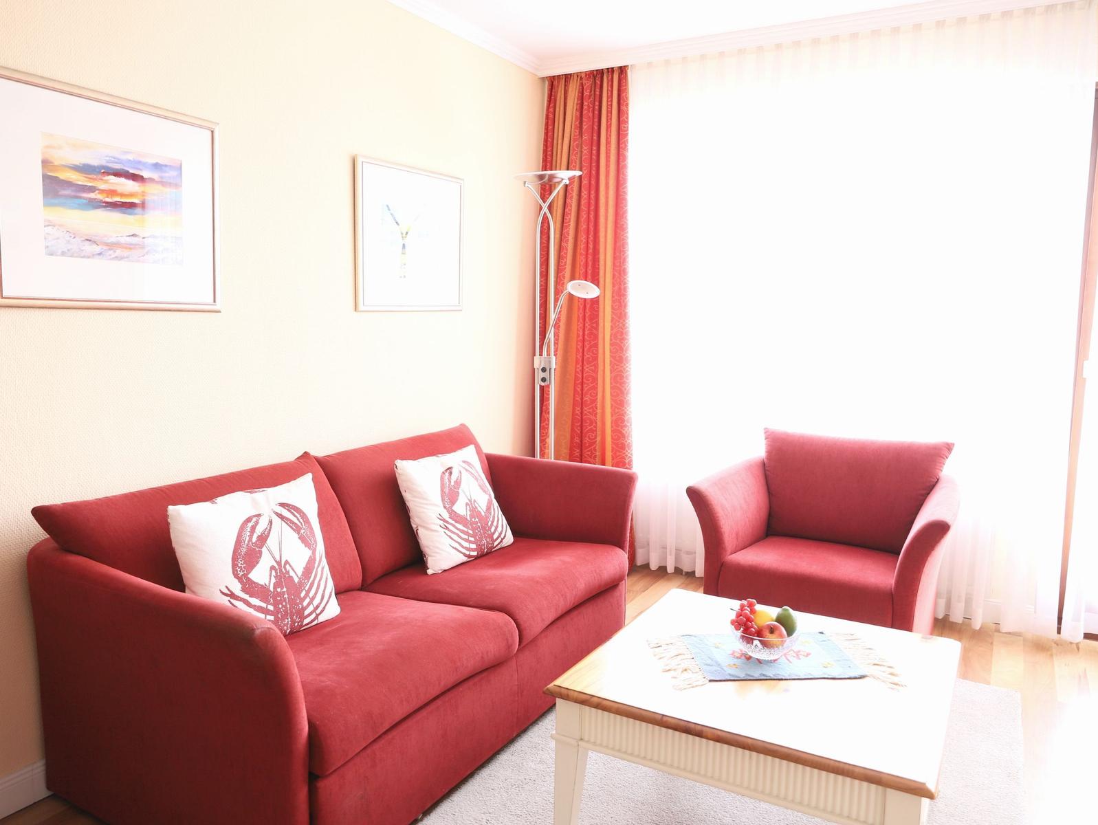 Ein Wohnzimmer mit rotem Sofa, einem Sessel und einem Tisch mit Obst.