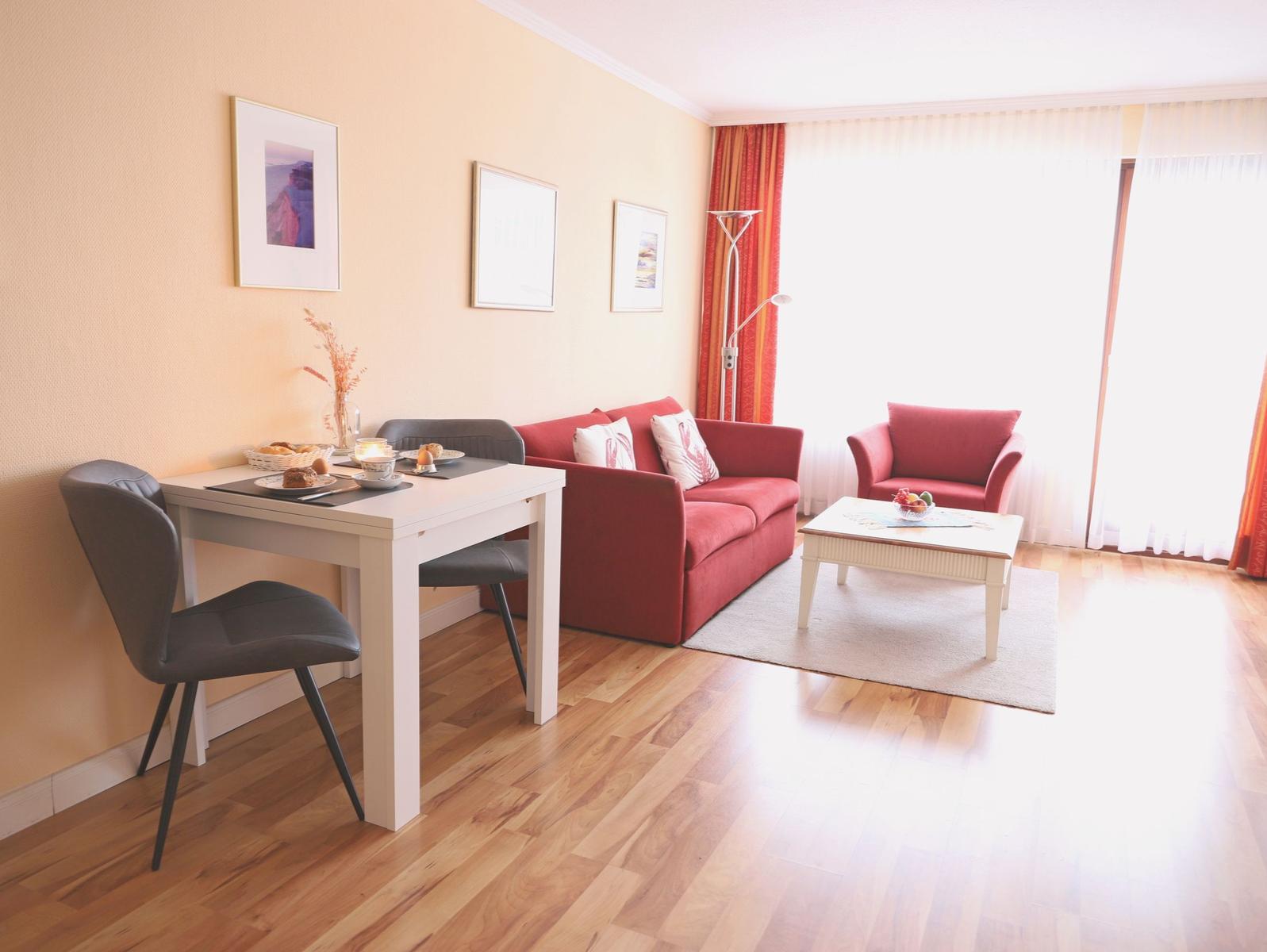 Wohn- und Essbereich mit rotem Sofa, weißen Möbeln und Holzboden.