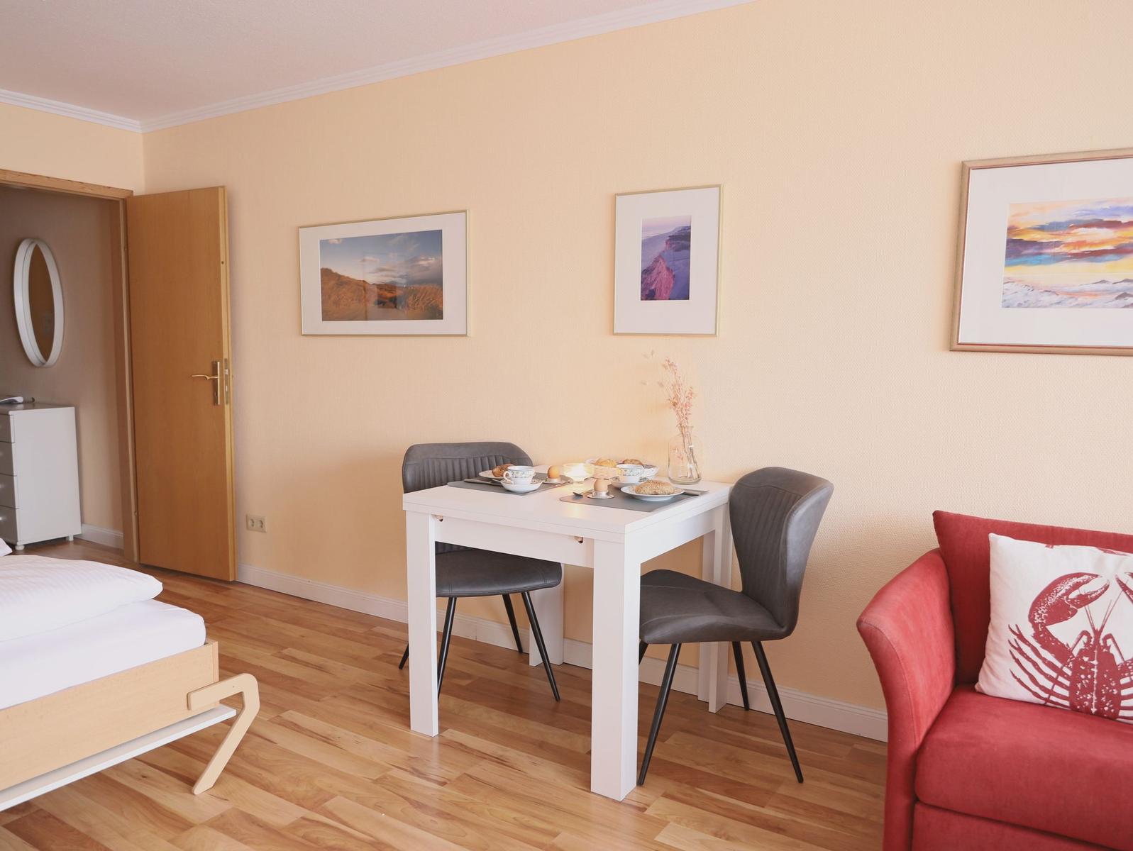 Ein Raum mit Esstisch, zwei Stühlen, rotem Sofa und Bildern an der Wand.