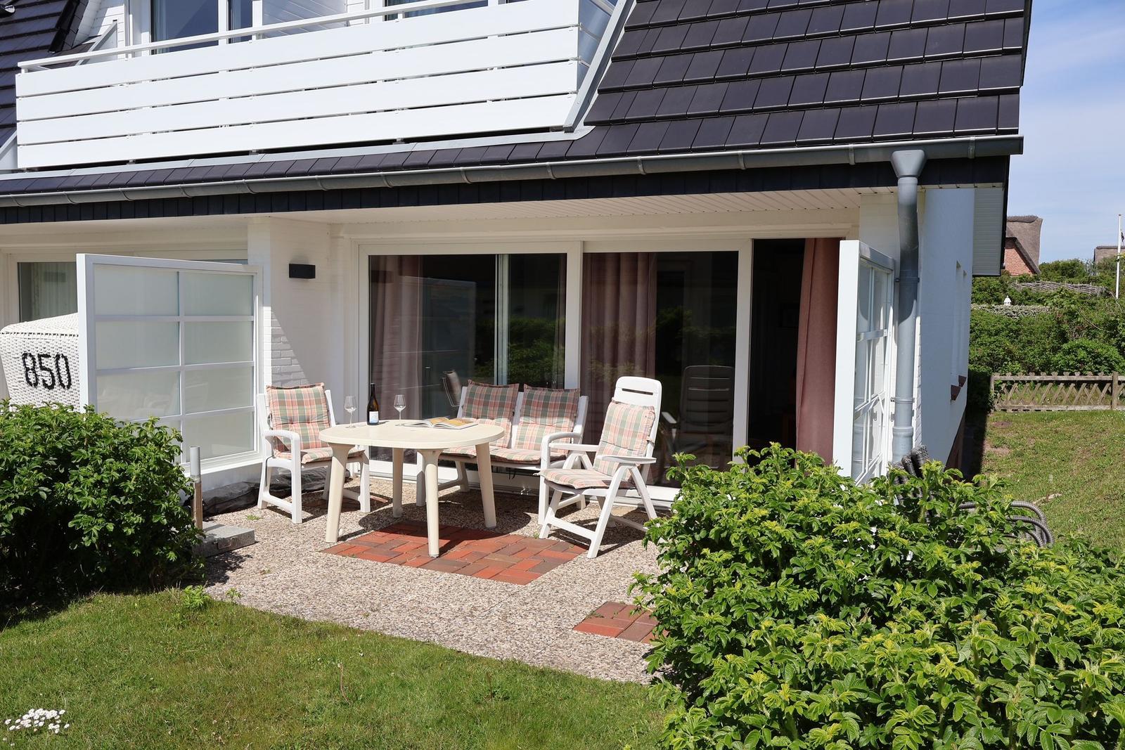 Terrasse mit Tisch, Stühlen und Grillbereich vor einem Haus mit Balkon.