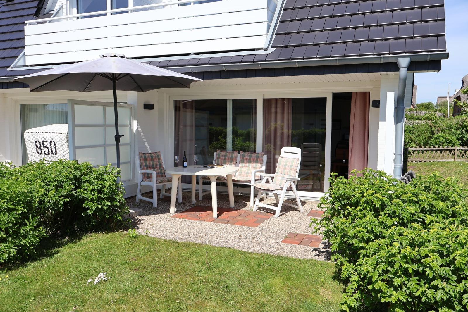 Terrasse mit Tisch, Stühlen und Sonnenschirm vor einem Haus mit Glasfront.