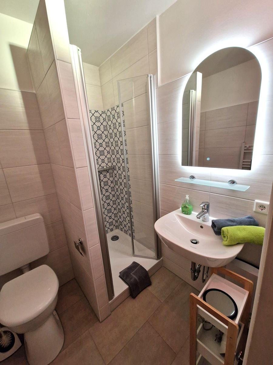 Badezimmer mit Dusche, Waschbecken und Toilette. Spiegel mit Beleuchtung und Handtücher.