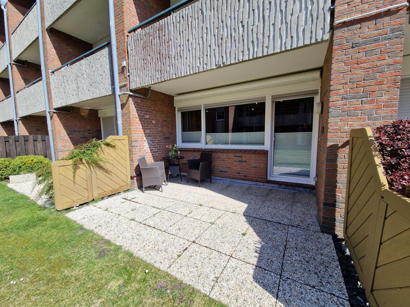 Terrasse mit Sitzgelegenheiten und Gartenbereich vor einem Mehrfamilienhaus.