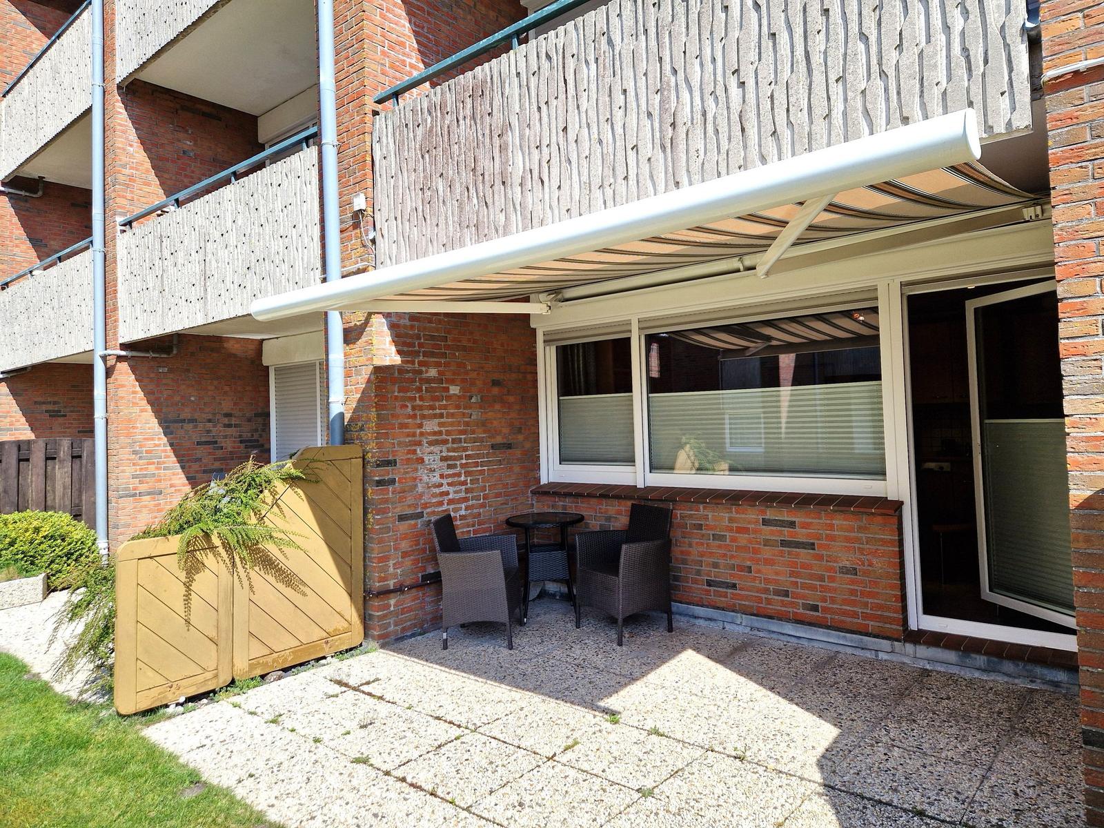 Terrasse mit Tisch und Stühlen unter Markise. Hinterhof mit Pflanzen und Steinplatten.