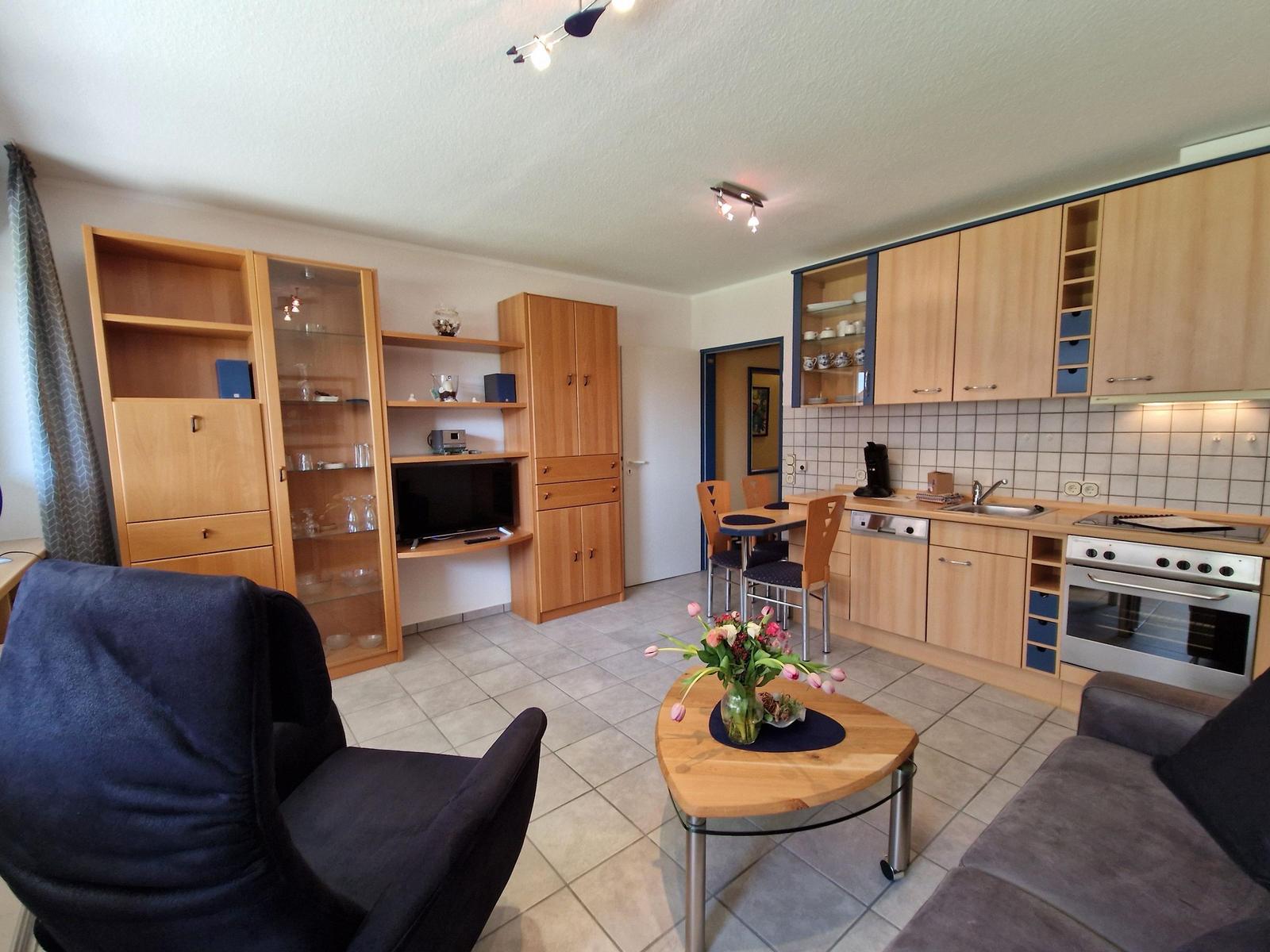 Wohnküche mit Holzmöbeln, Esstisch, Kühlschrank und Kochfeld.
