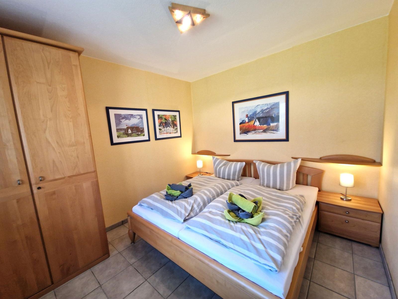 Schlafzimmer mit Doppelbett, Holzmöbel und Wandbildern.