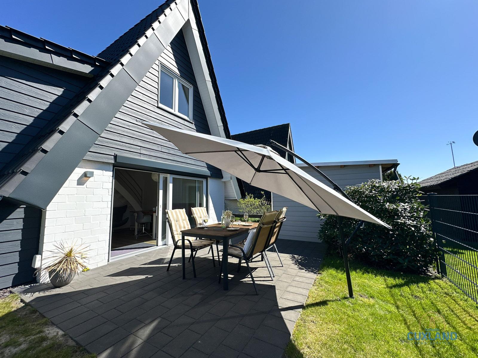 Terrasse mit Tisch, Stühlen und Sonnenschutz vor modernem Haus.