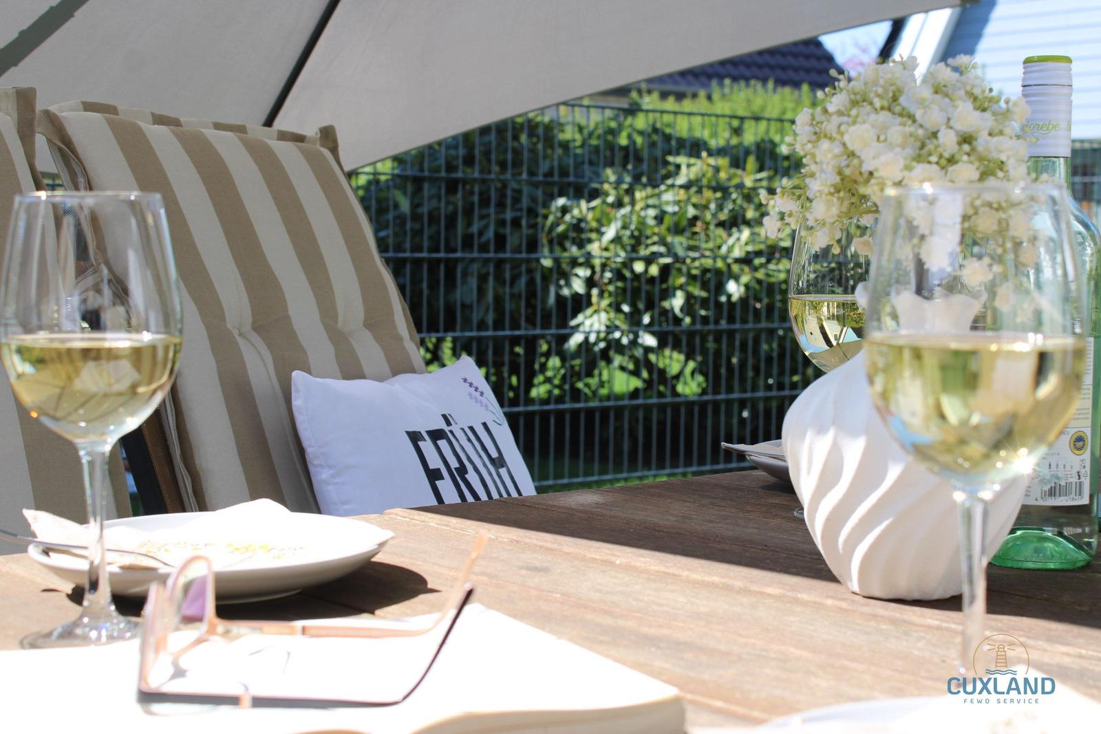 Außenbereich mit Tisch, Stühlen, Wein und Blumen unter Sonnenschutz.