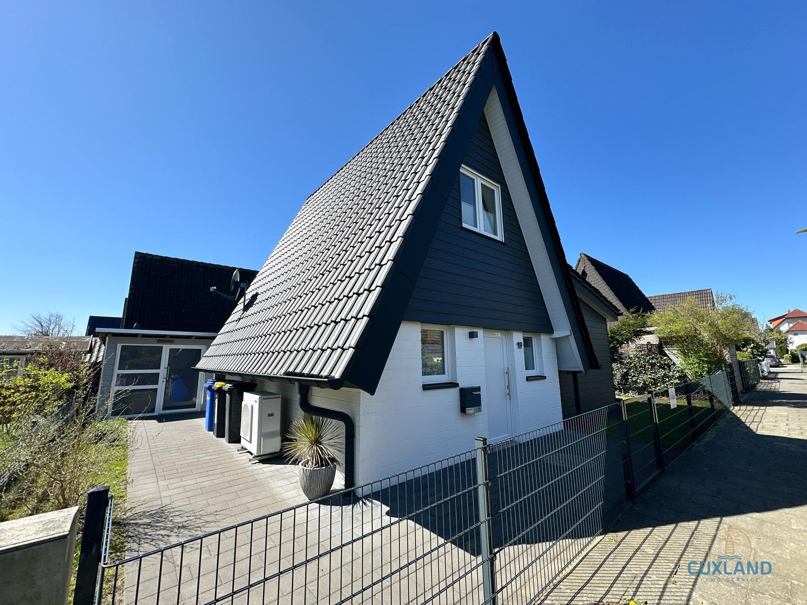 Modernes Haus mit schwarz-weißem Fassaden und Dach aus Ziegeln. Vorgarten mit Zaun und Pflanzen.