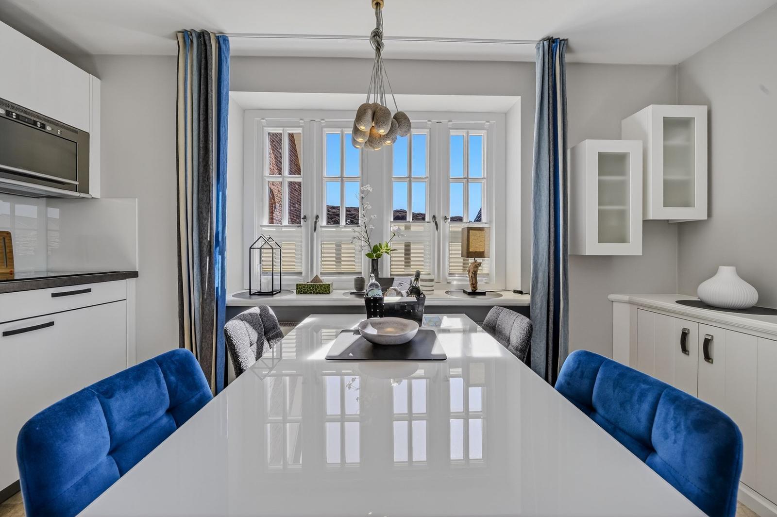 Essbereich mit weißem Tisch und blauen Stühlen, Fenster mit Blick auf Gebäude.