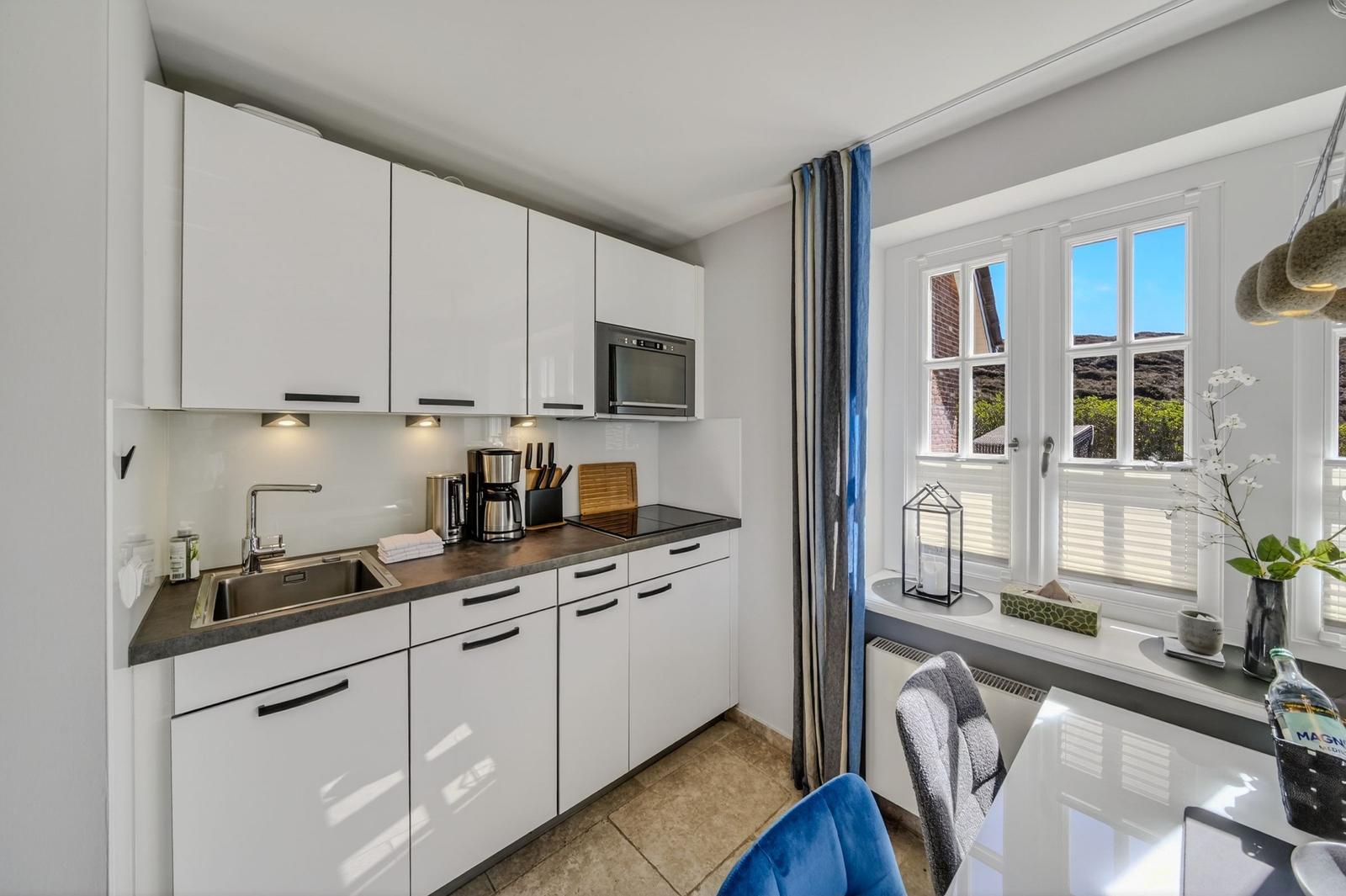 Küche mit weißen Schränken, Arbeitsplatte und Fenster mit Blick nach draußen.