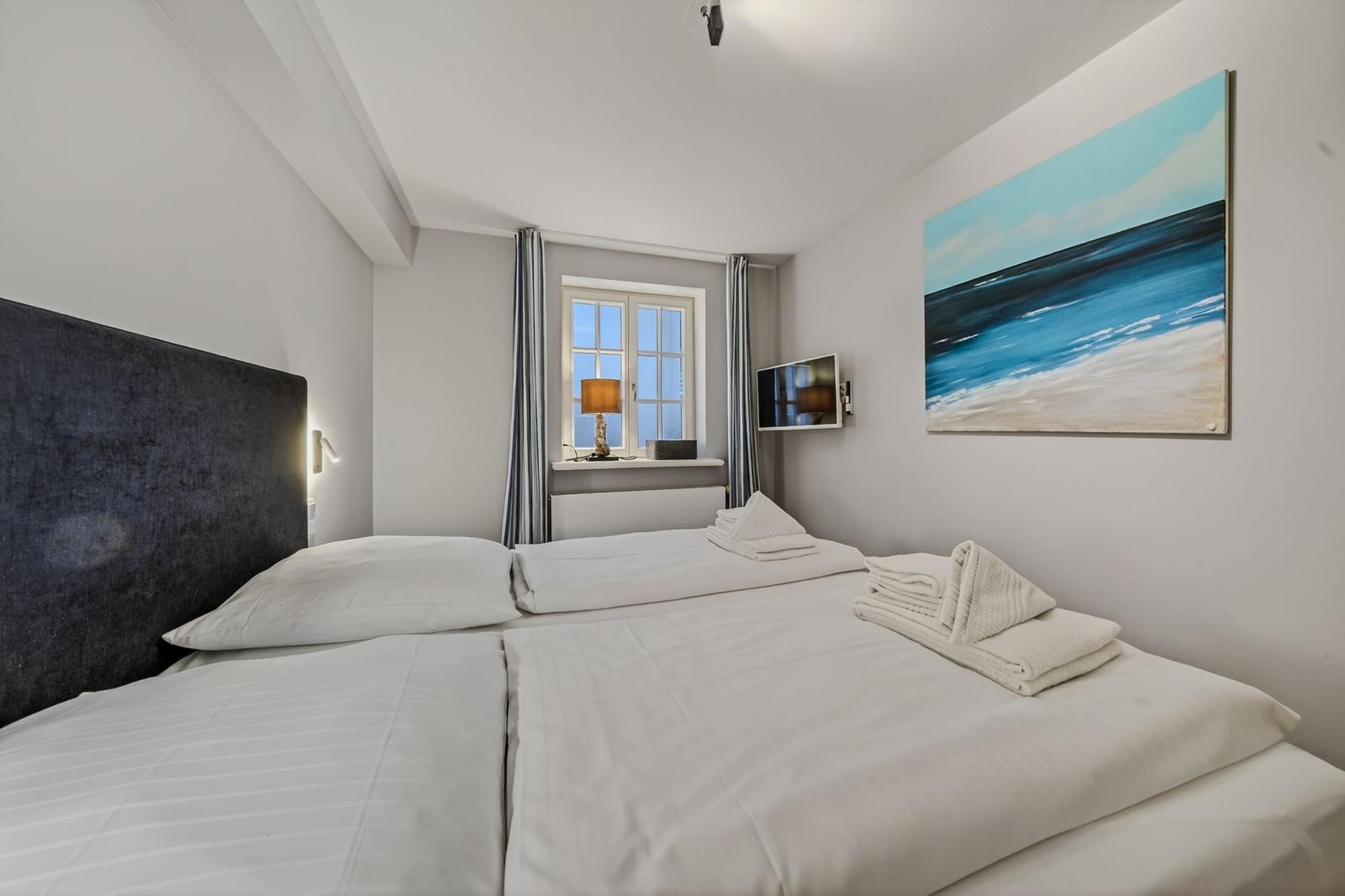 Schlafzimmer mit Doppelbett, Fenster, Wandbild und TV.