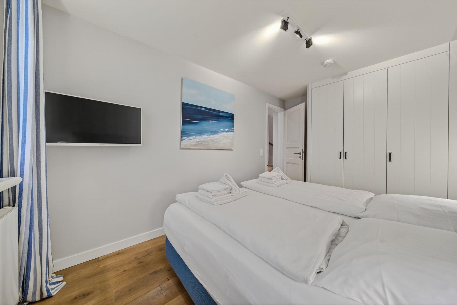 Schlafzimmer mit Doppelbett, Kleiderschrank und Wandbild. Fernseher an der Wand.