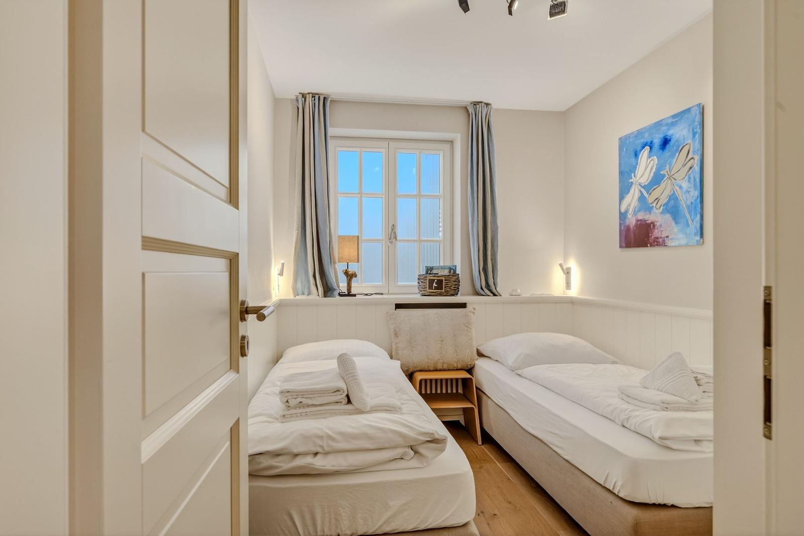 Zwei Einzelbetten, Fenster mit Vorhängen, Wandbild mit Libellen, Holzboden und Nachttisch.