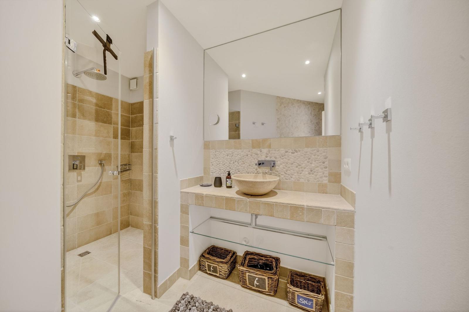 Dusche mit Glaswand, Waschbecken mit Spiegel und Körbe unter der Ablage.