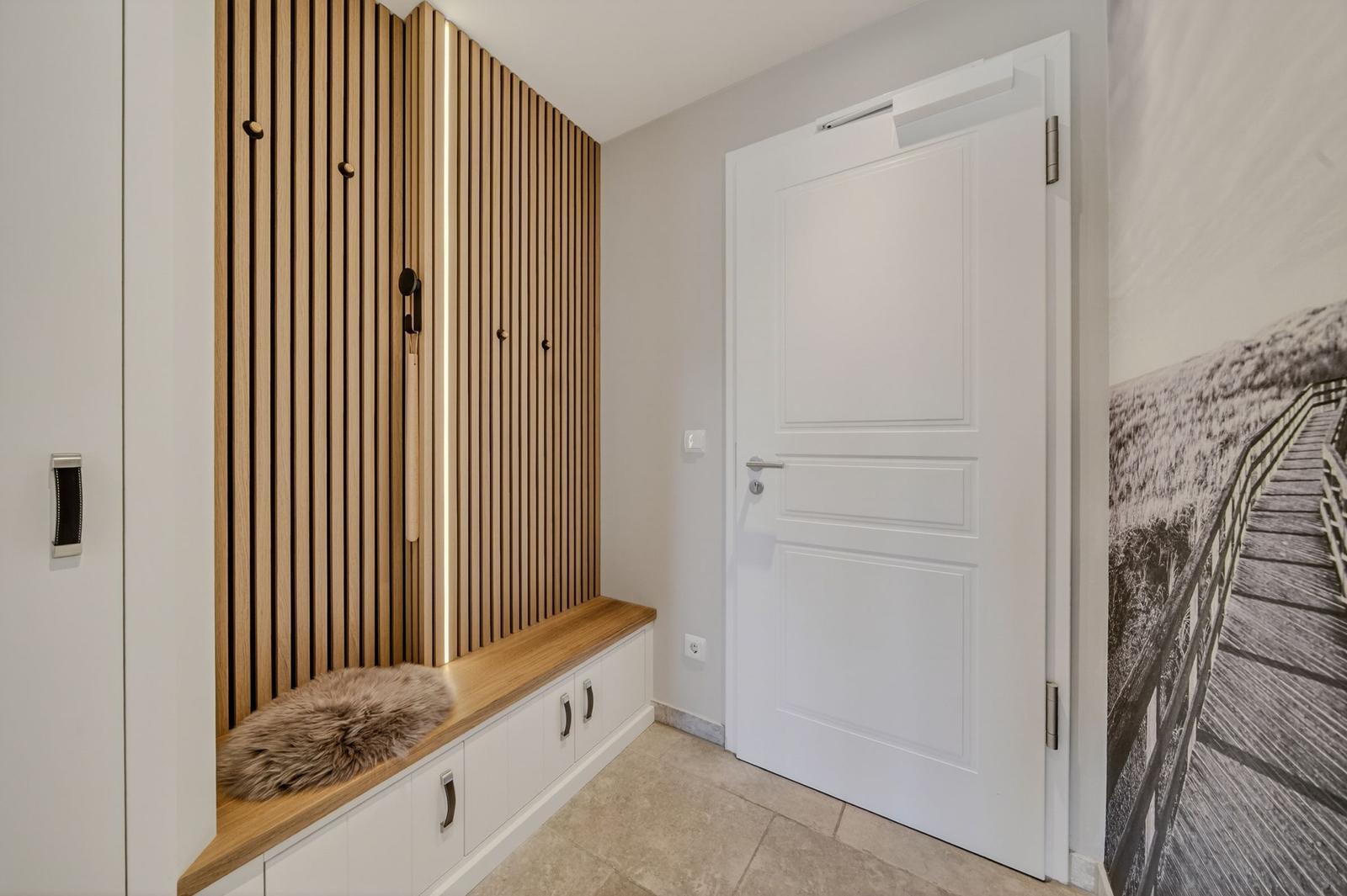 Eingangsbereich mit Holzwand, Sitzbank und weißer Tür.