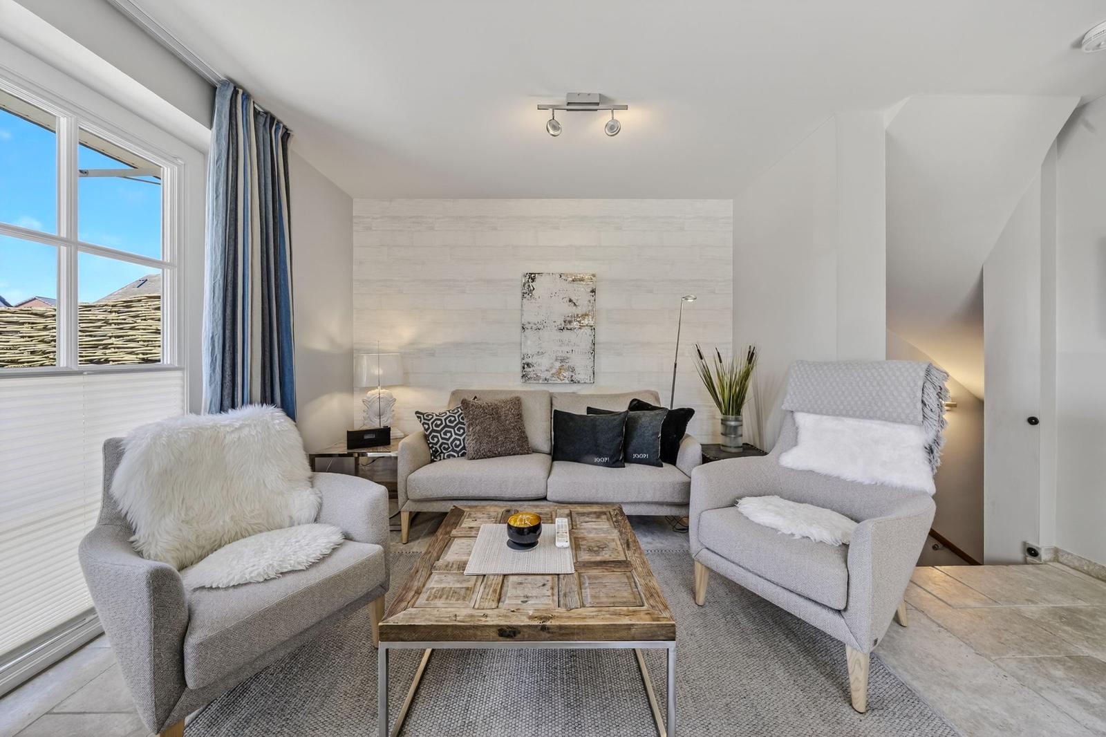Wohnzimmer mit Sofa, zwei Sesseln, Holztisch und Fenster mit Blick.