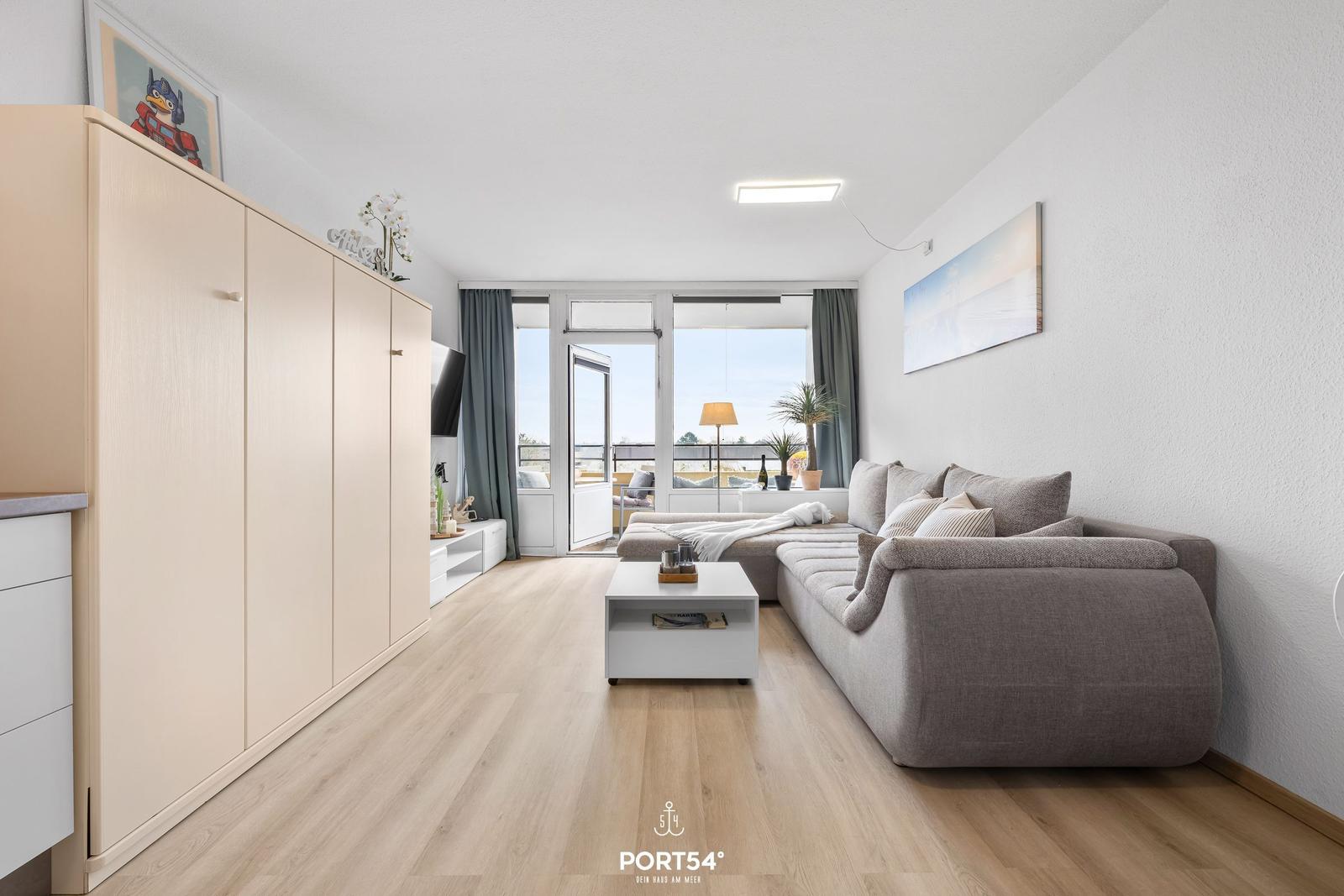 Wohnzimmer mit grauem Sofa, weißem Couchtisch und Holzboden. Durchgang zur Terrasse mit Blick.