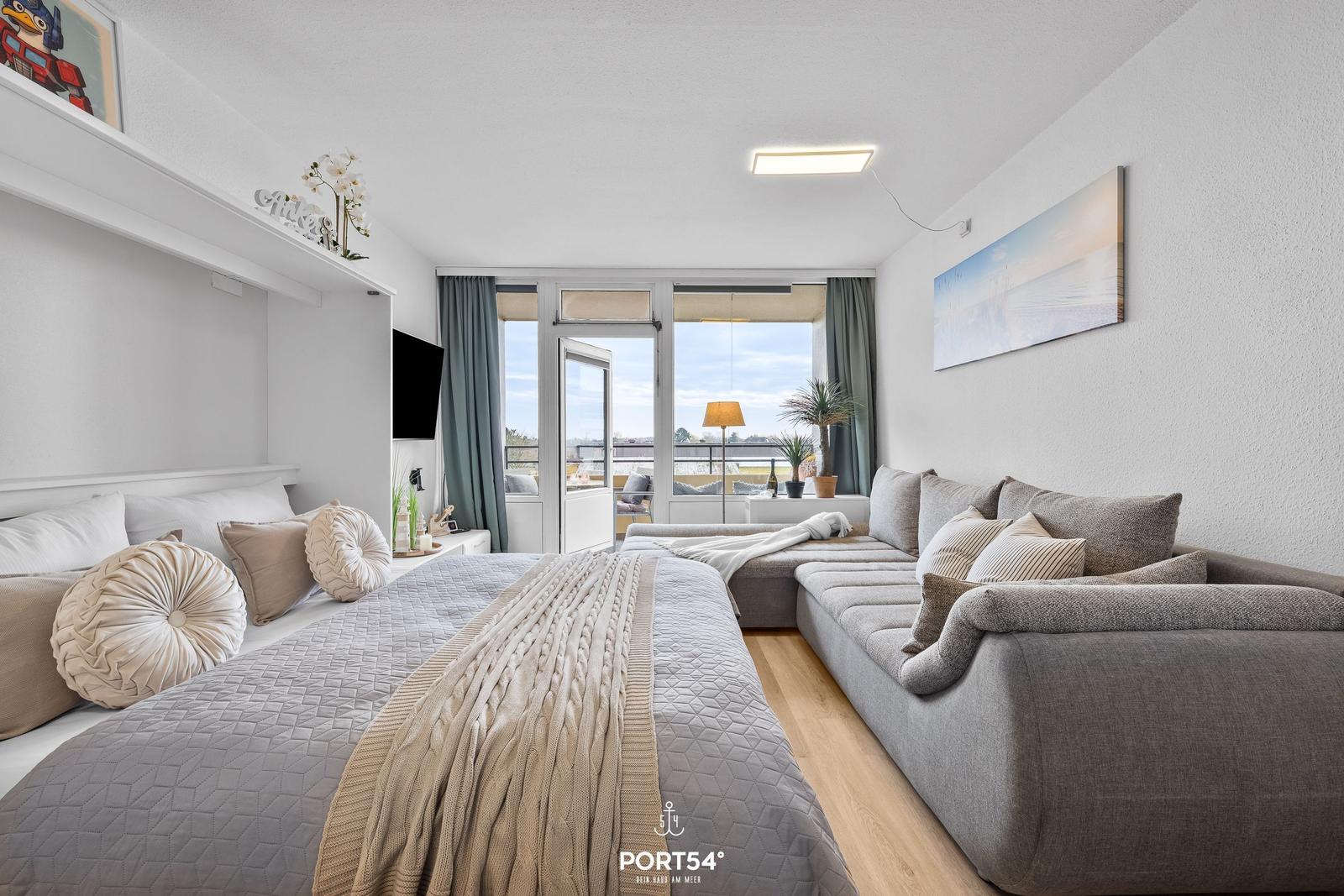 Schlafzimmer mit Bett, Sofa und Balkonansicht. Wandbild und TV sichtbar.