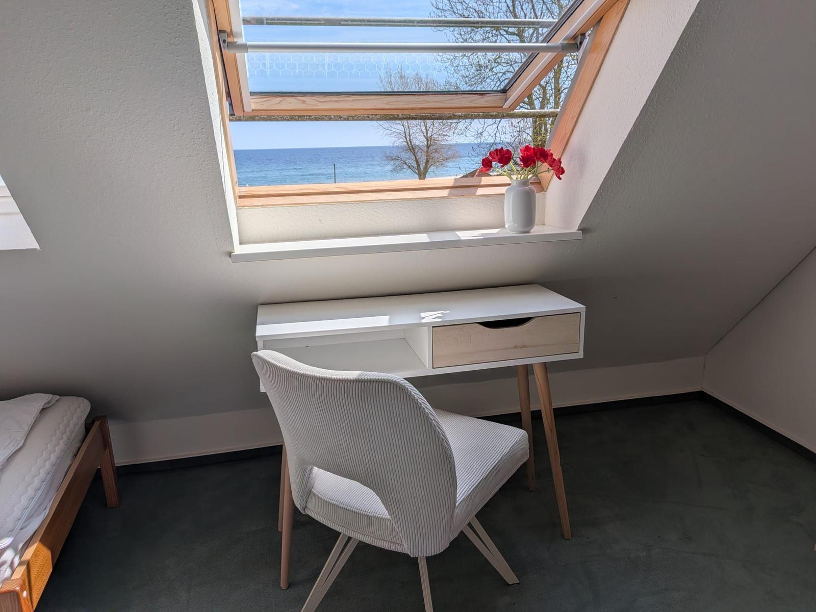 Schlafzimmer mit Schreibtisch und Blick aufs Meer durch Dachfenster.