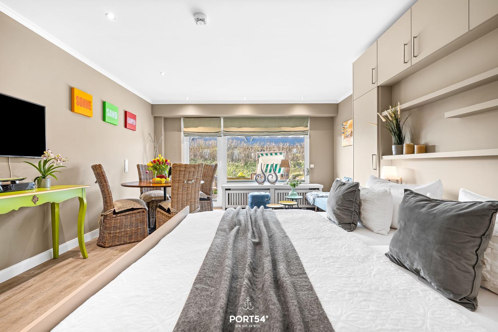 Bedroom with large bed, window view, and dining area with chairs.
