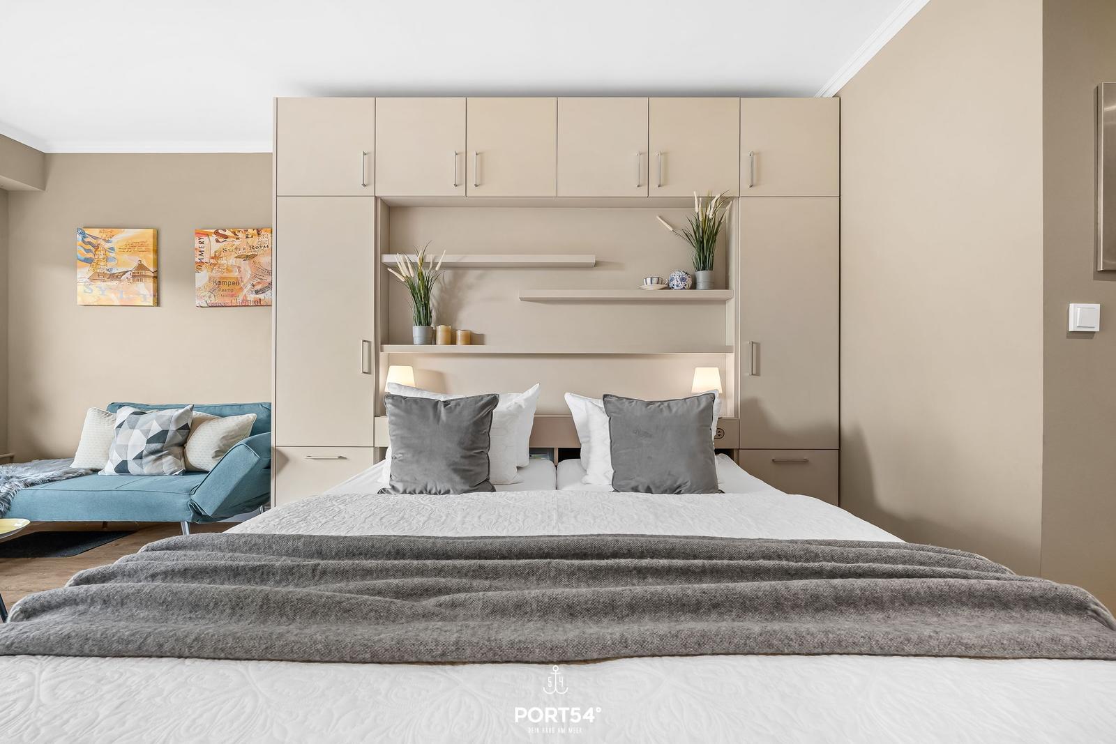 Bedroom with bed, nightstands, and integrated wardrobe. Blue sofa and wall art are visible.