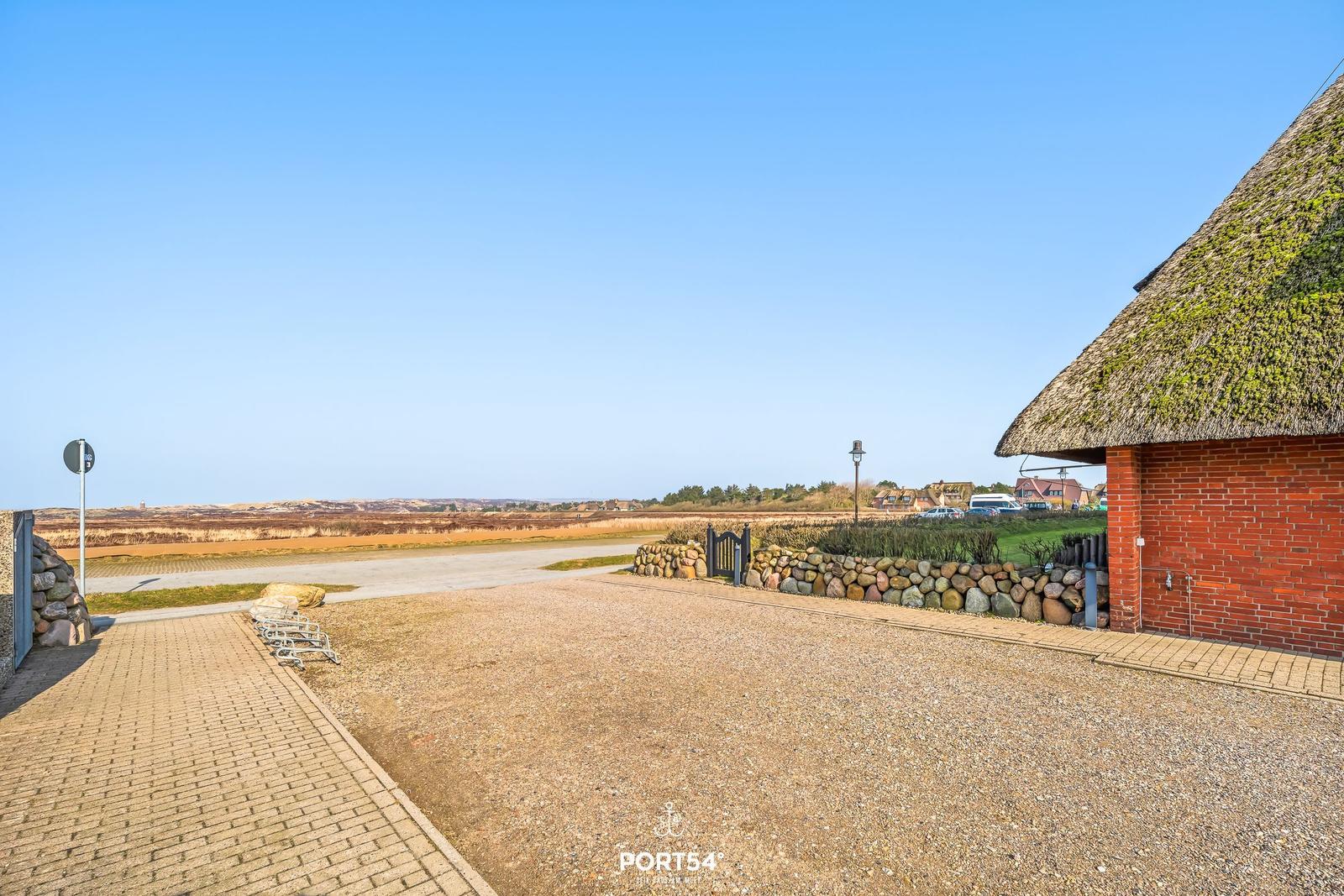 House with thatched roof and stone wall. View of fields and sky.