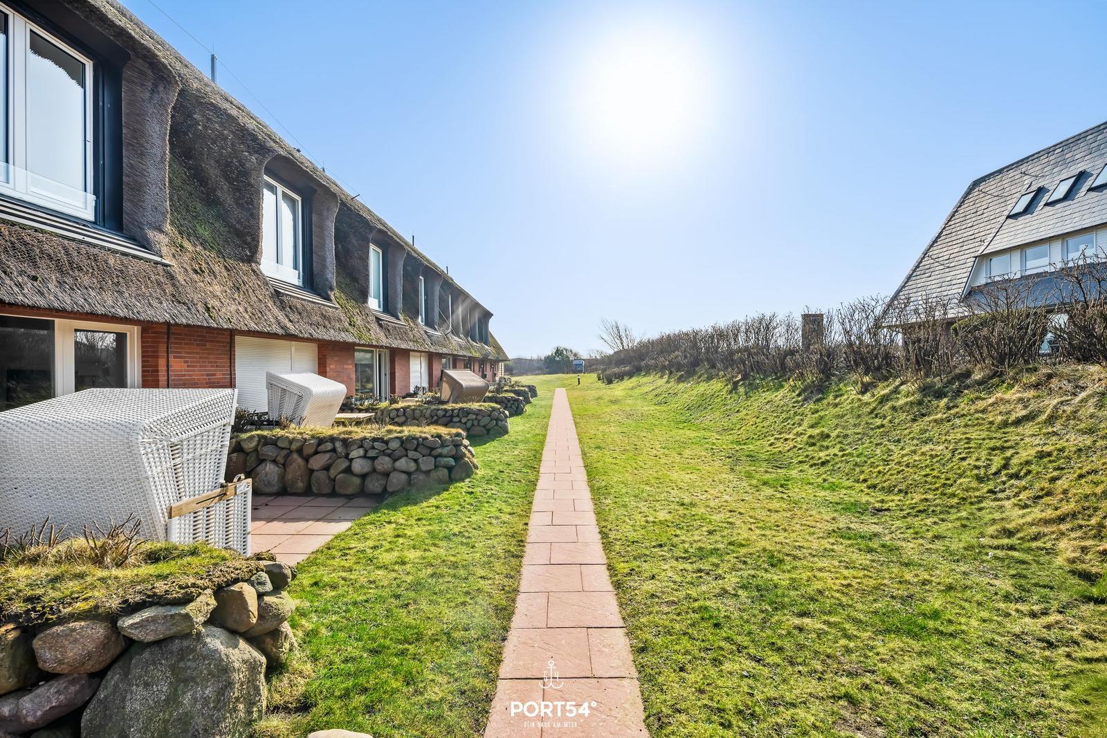 A paved path leads between green areas and houses with thatched roofs.