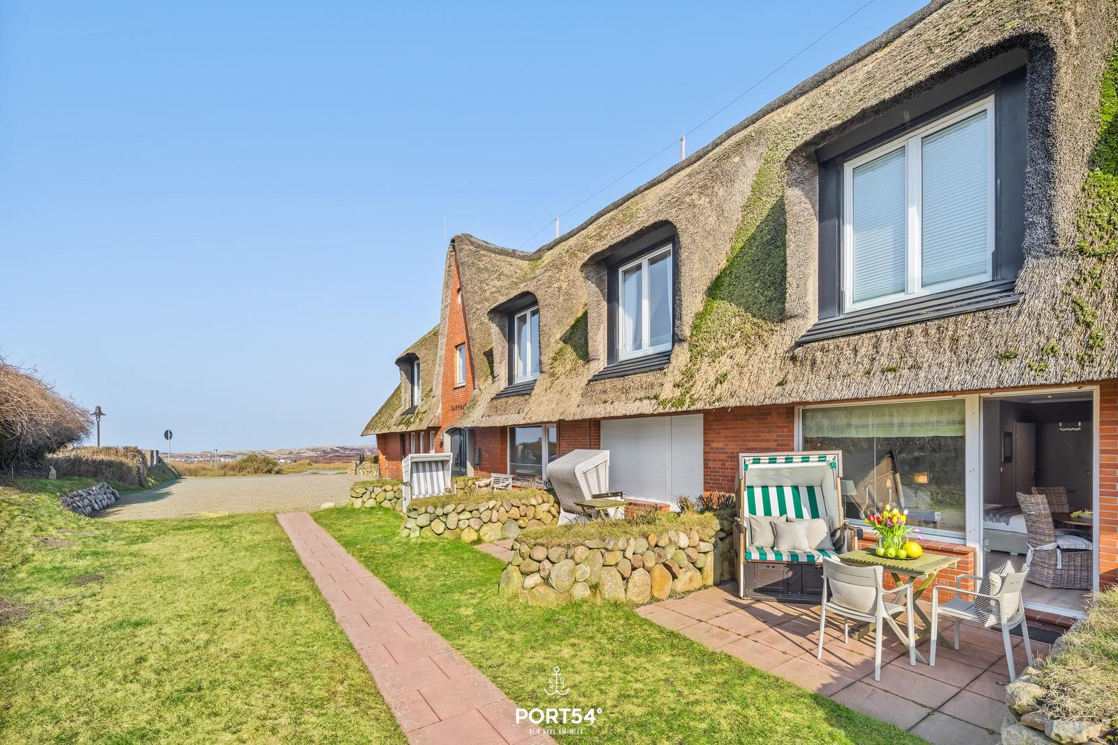 House with thatched roof, terrace with seating and view of grassy area.