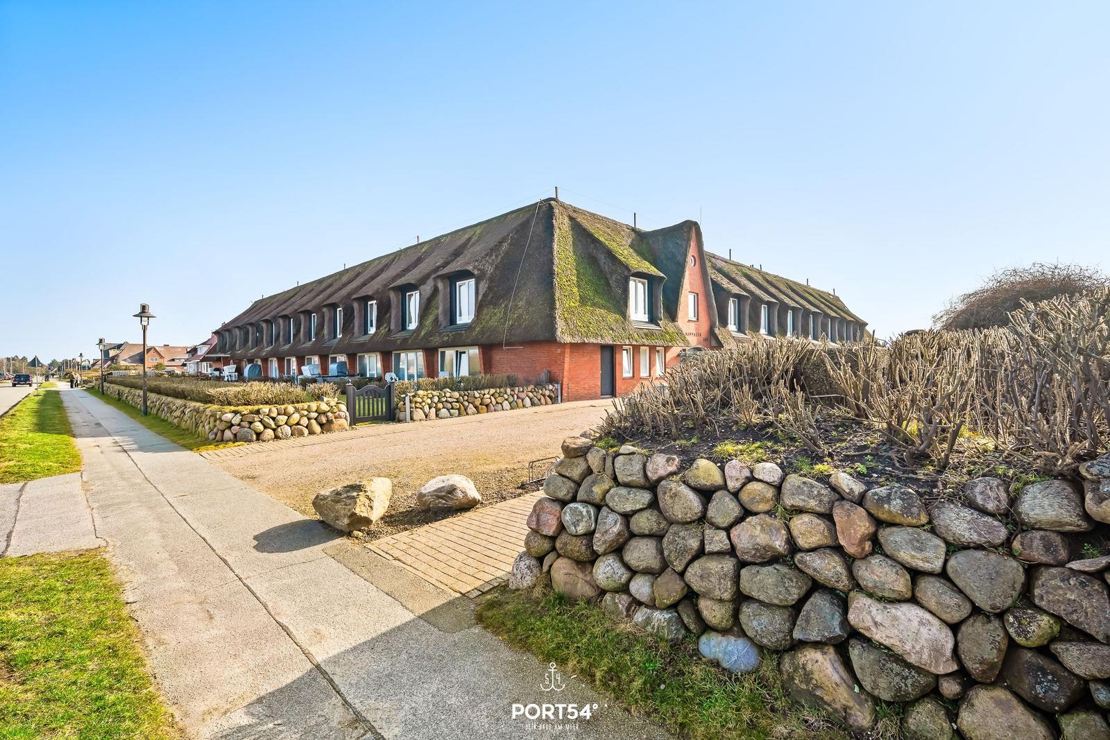Row house with thatched roof and stone wall along the path.